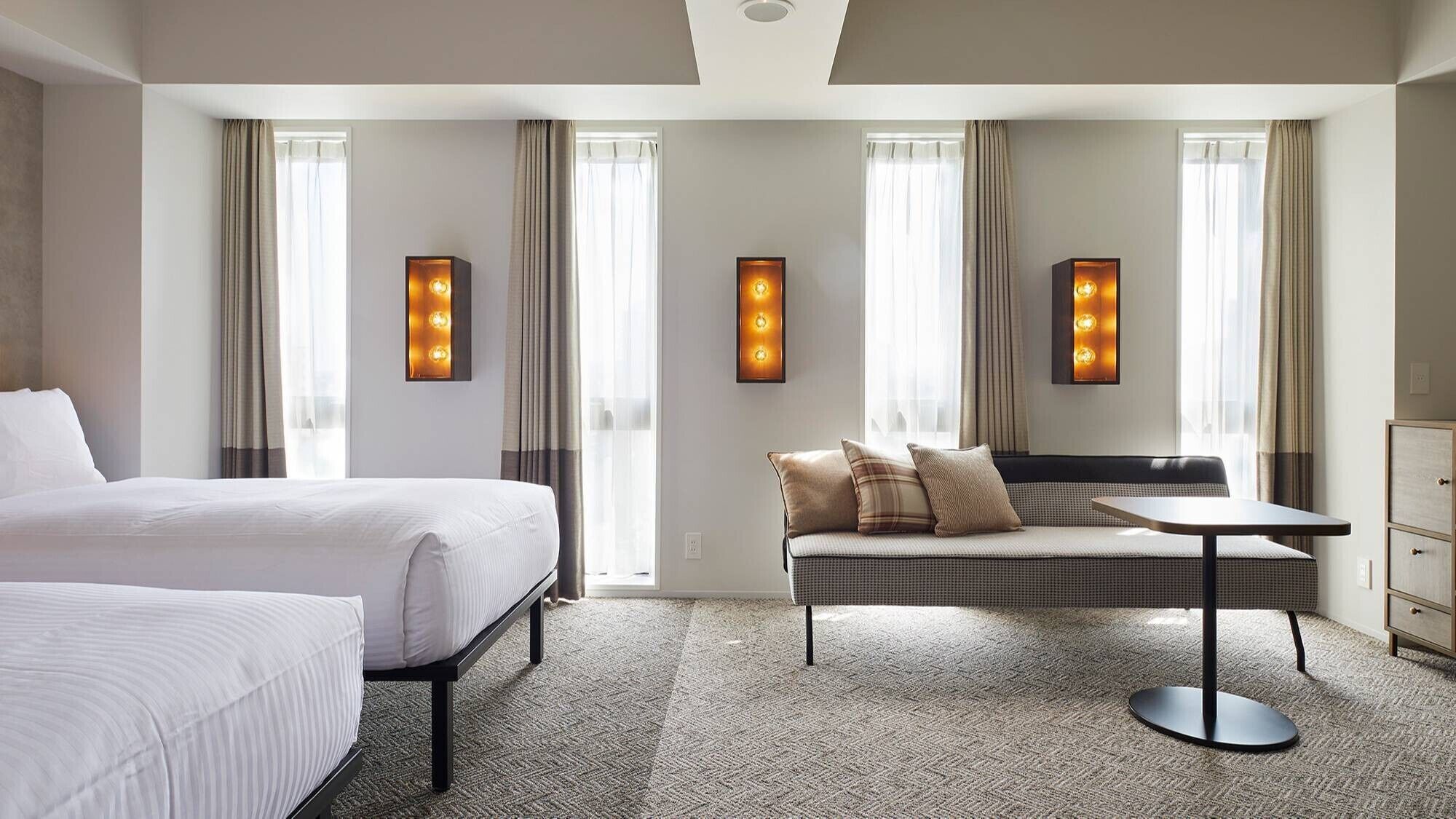 Habitación de hotel con cama, sofá, mesa e iluminación en la pared.