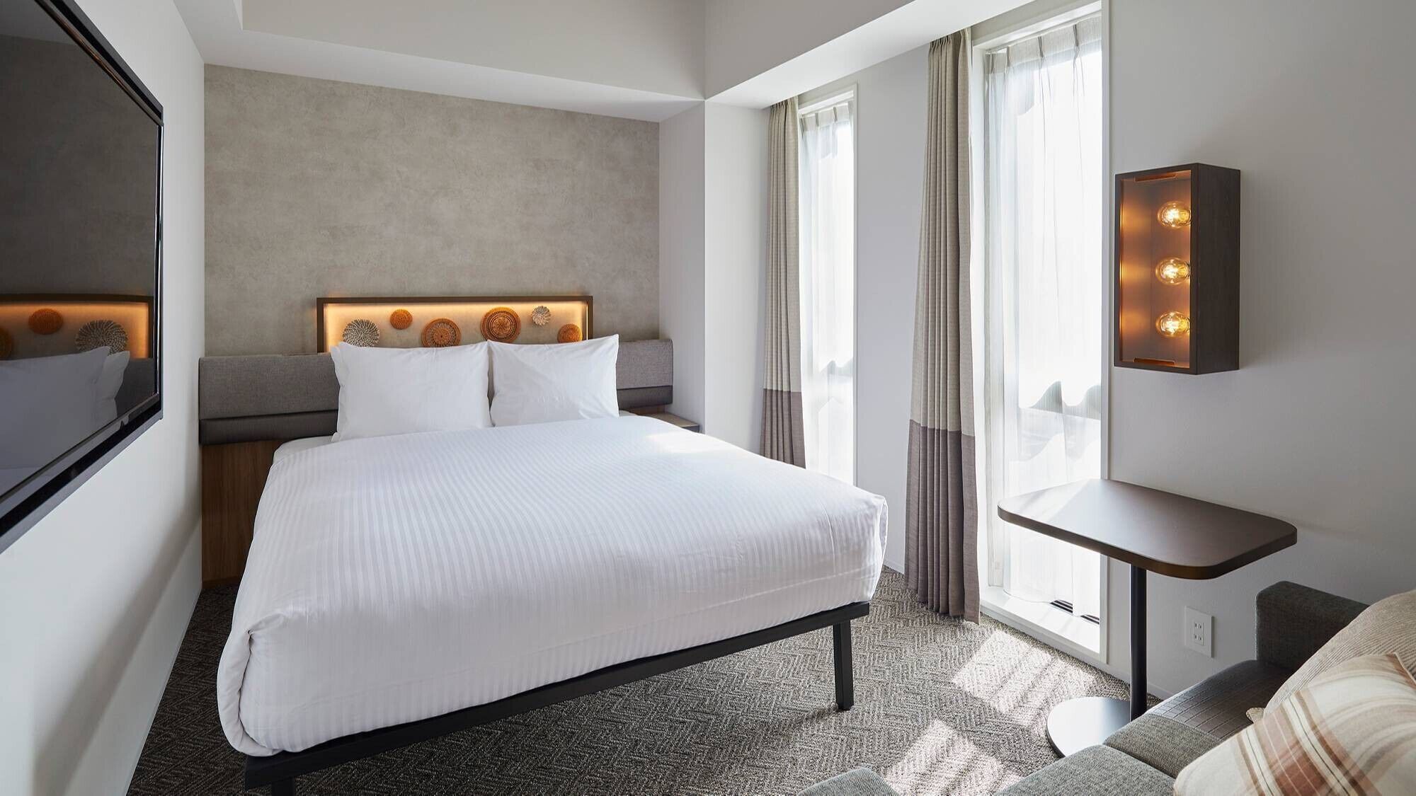 Una habitación de hotel con una cama grande, una mesita de noche, un espejo y una ventana con cortinas.