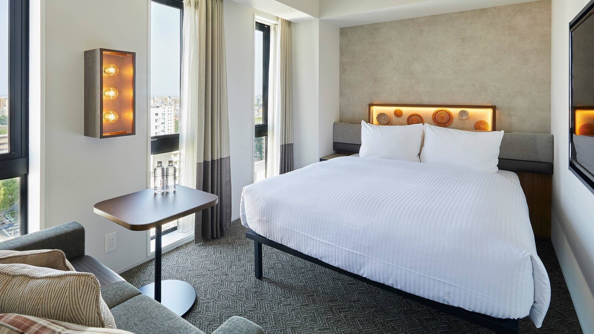 Habitación de hotel con una cama grande, una mesita, un sofá y vistas a la ciudad desde la ventana.