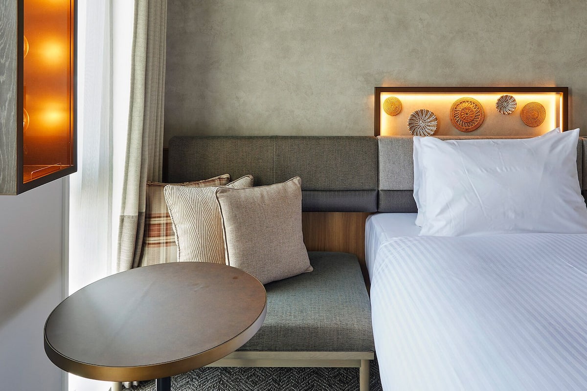 Hotellihuone, jossa on sänky, yöpöytä, koristevaloilla varustettu sängynpääty ja näkymä ulos.