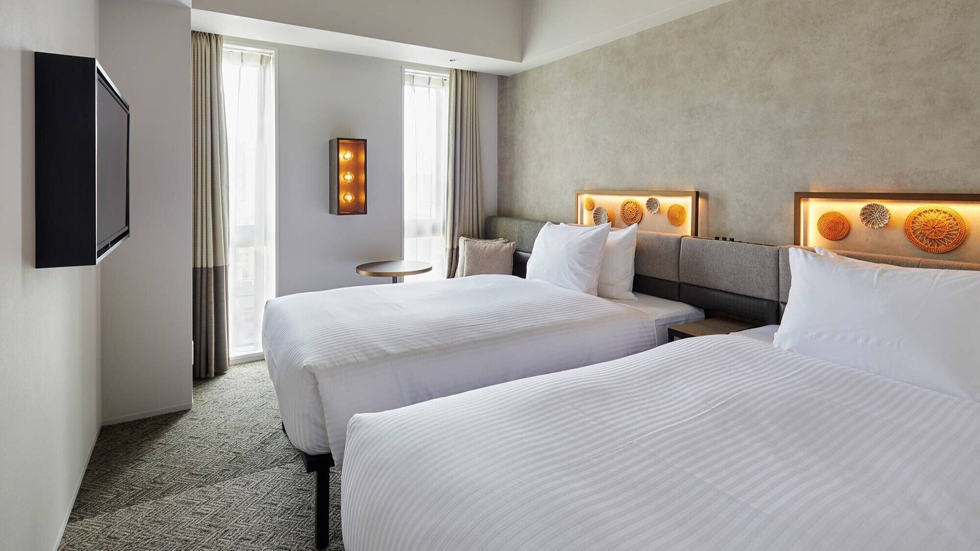 Una habitación de hotel con dos camas, un televisor, un cabecero con luces y una ventana con cortinas.