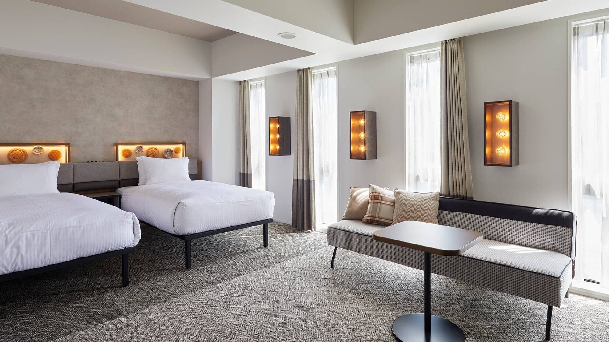 Habitación de hotel con dos camas, un sofá, una mesita y luces instaladas en la pared.