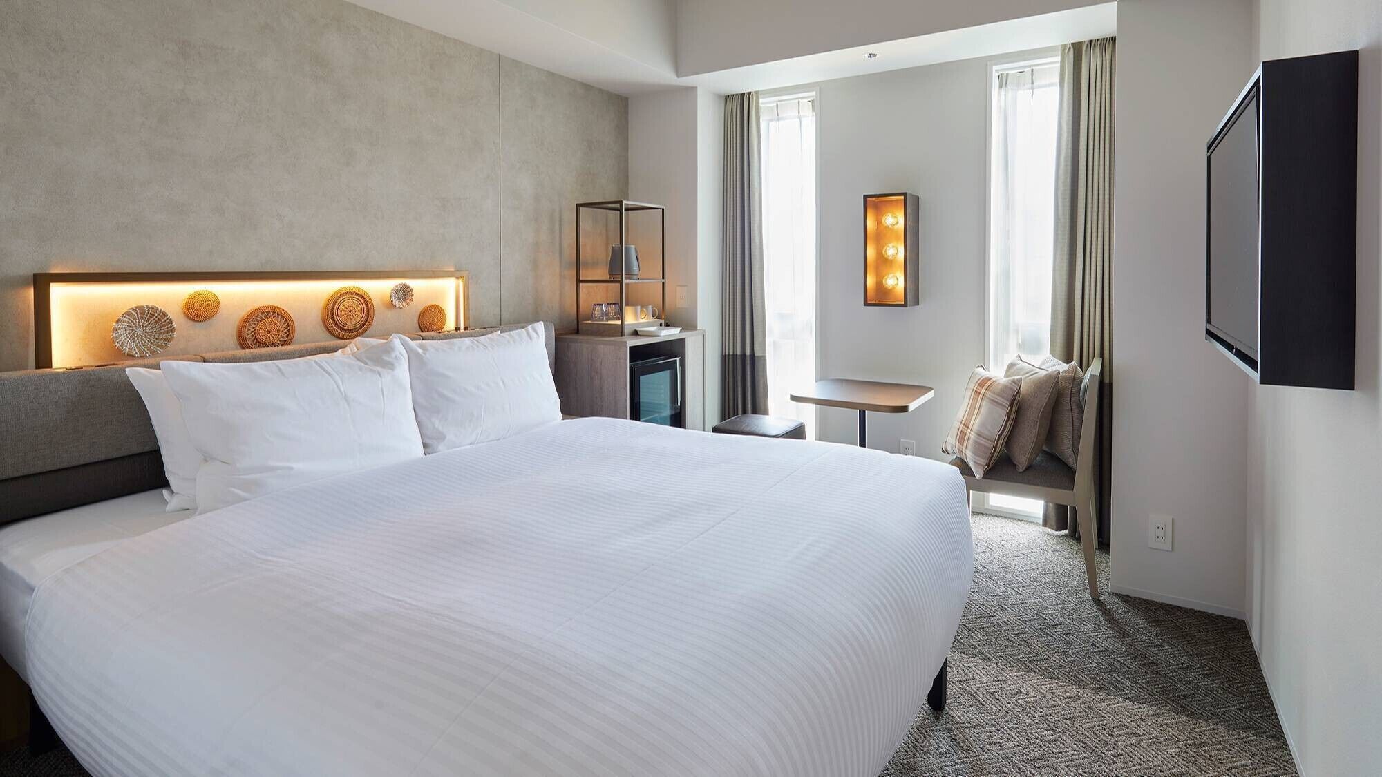 Habitación de hotel con una cama grande, un escritorio, una silla, un televisor y un ventanal con cortinas.