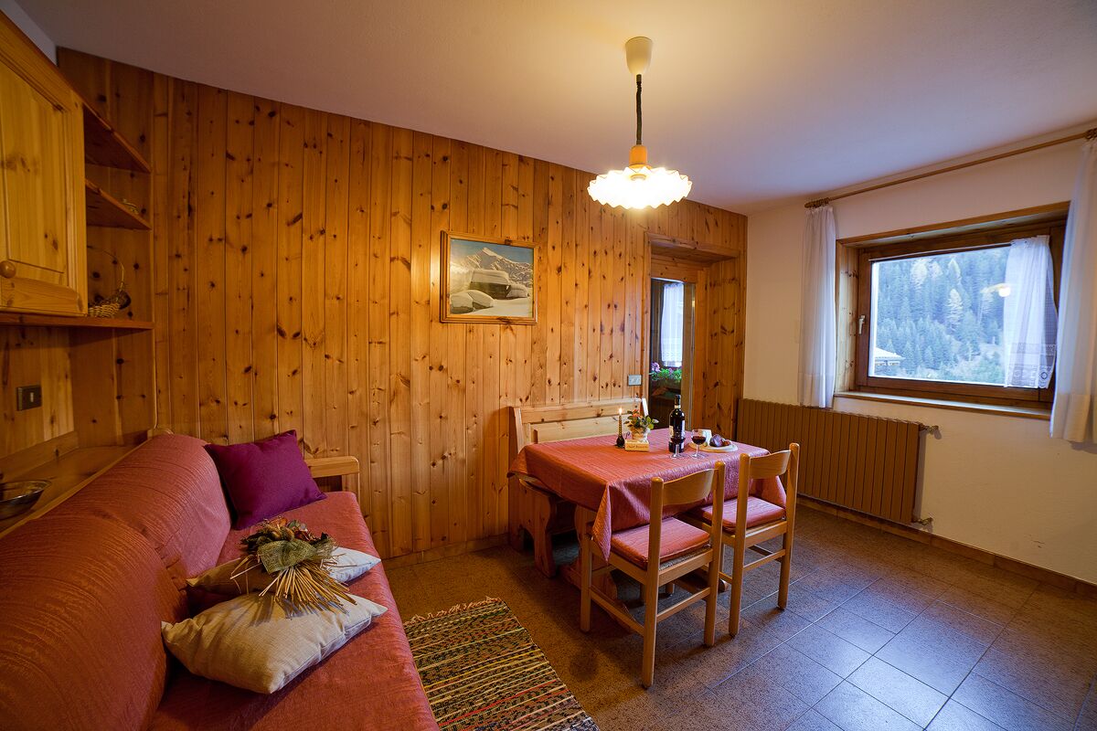 Ein gemütliches Holzhaus-Interieur mit einer Holzwand, einem Esstisch mit Stühlen, einer Couch und einem Fenster mit Blick auf Bäume.
