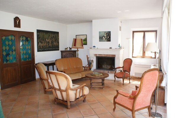 A living room with a fireplace, a sofa, two armchairs, a coffee table, and a dining table. - A peaceful vacation on a large property in the heart of the Pays de Fayence. (TOURRETTES)