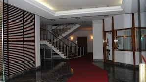 Un'hall d'albergo con tappeto rosso, una scala e un parete di legno con listelli orizzontali.
