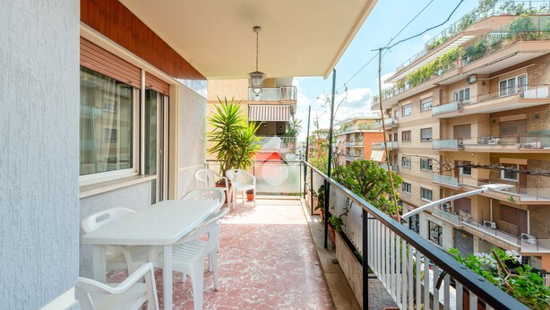 Un balcone con tavolo e sedie, piante in vaso e vista sugli edifici vicini.