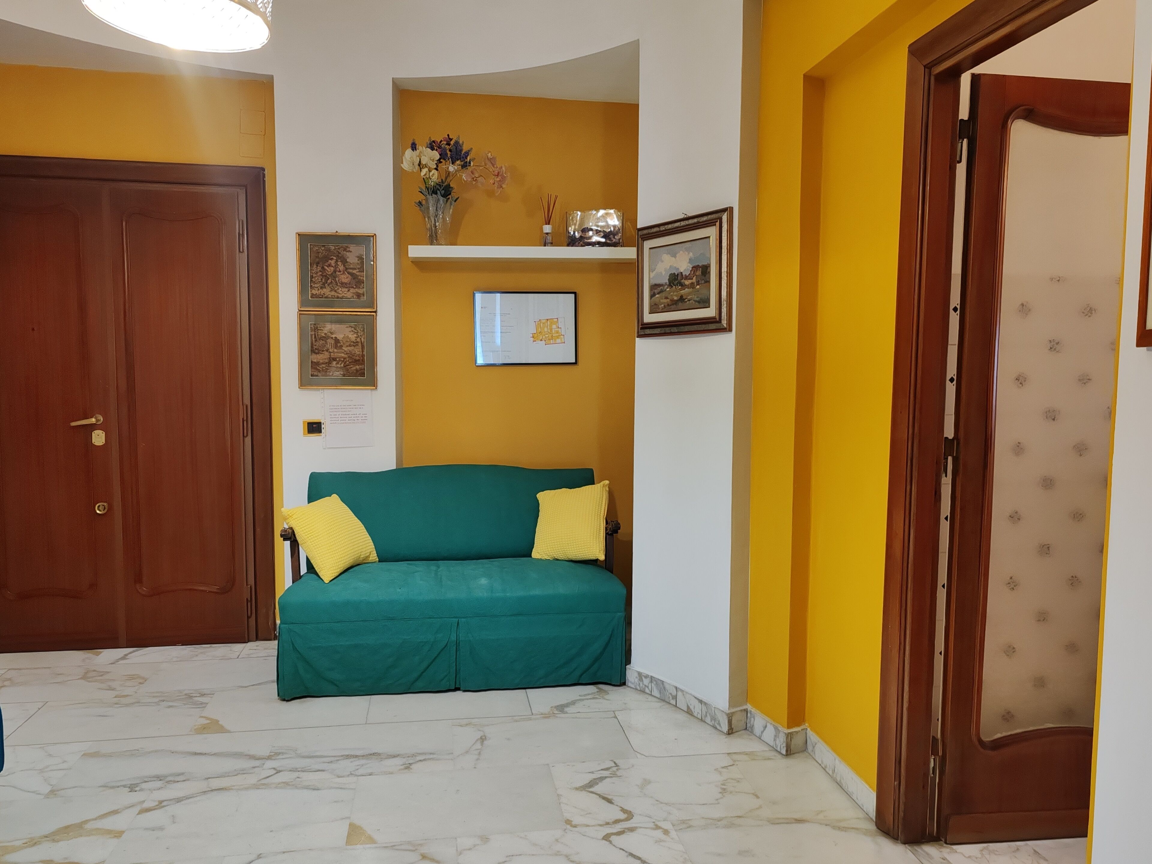 Ein Zimmer mit einem grünen Sofa, einer Holztür, einer gelben Wand und einem gerahmten Bild.