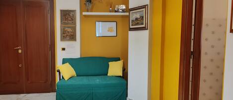 Ein Zimmer mit einem grünen Sofa, einer Holztür, einer gelben Wand und einem gerahmten Bild.