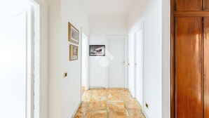 Un corridoio con pavimento decorato, pareti bianche e una porta in legno sulla destra.