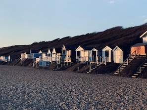 Een rij strandhutten met trappen die erheen leiden, gelegen op een kiezelstrand.