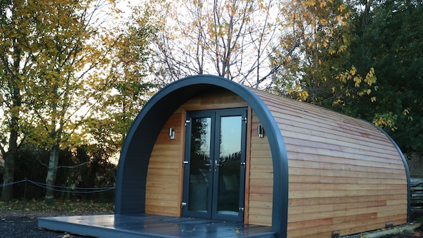 A modern, semi-circular wooden structure with a glass door and a small platform in front. - Glampods - 5 Berth Glamping Pod Elgin (Elgin)
