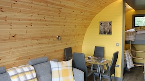 A cozy room with a wooden ceiling, a dining area with a table and chairs, a sofa with a plaid throw, and a bunk bed with a plaid blanket. - Glampods - 5 Berth Glamping Pod Elgin (Elgin)