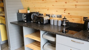 A kitchen with a wooden wall, a black countertop, and various appliances including a coffee maker, toaster, and kettle. - Glampods - 5 Berth Glamping Pod Elgin (Elgin)