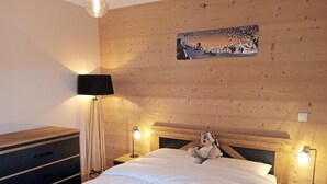 A bedroom with a wooden headboard, a bed with white bedding, a nightstand with a lamp, and a dresser. - Cozy Apartment in Châtel, 6 Pers. (Châtel)