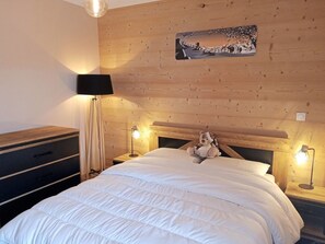 Ein Schlafzimmer mit einem hölzernen Kopfende, einem Bett mit weißer Bettwäsche, einem Nachttisch mit Lampe und einer Kommode.
