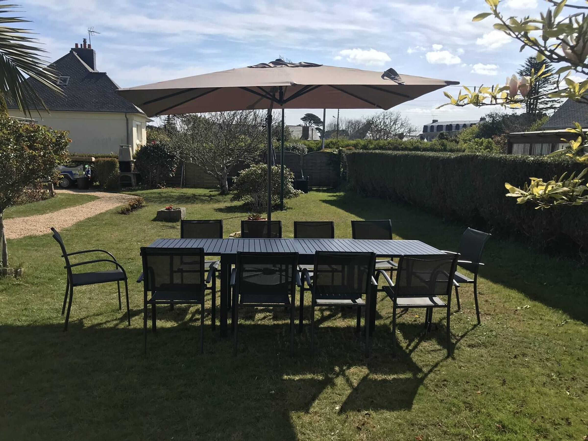 Een terras met een tafel en stoelen, omgeven door een haag en een huis op de achtergrond.