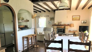 Un salon chaleureux avec une cheminée, un coin repas avec des chaises en bois, une cuisine avec un bar et un téléviseur.