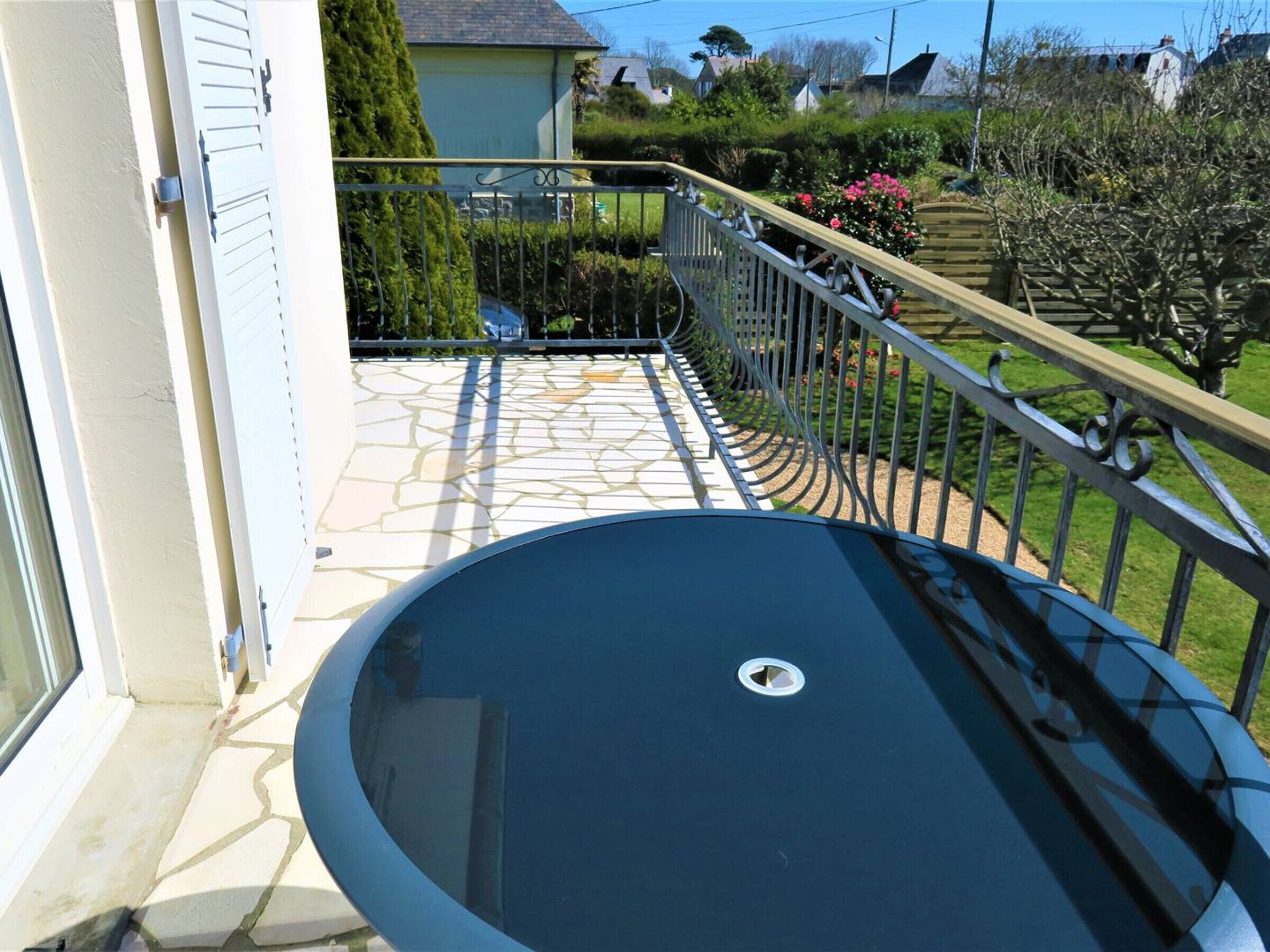 A circular outdoor pool with a metal railing, surrounded by a stone patio and a garden with various plants and flowers.