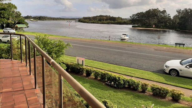 A view from a balcony overlooking a river with a boat, cars, and greenery. - Braemar Unit 3 (Forster)