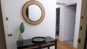 A hallway with a black console table, a round mirror with a woven frame, and a green plant. - Braemar Unit 3 (Forster)