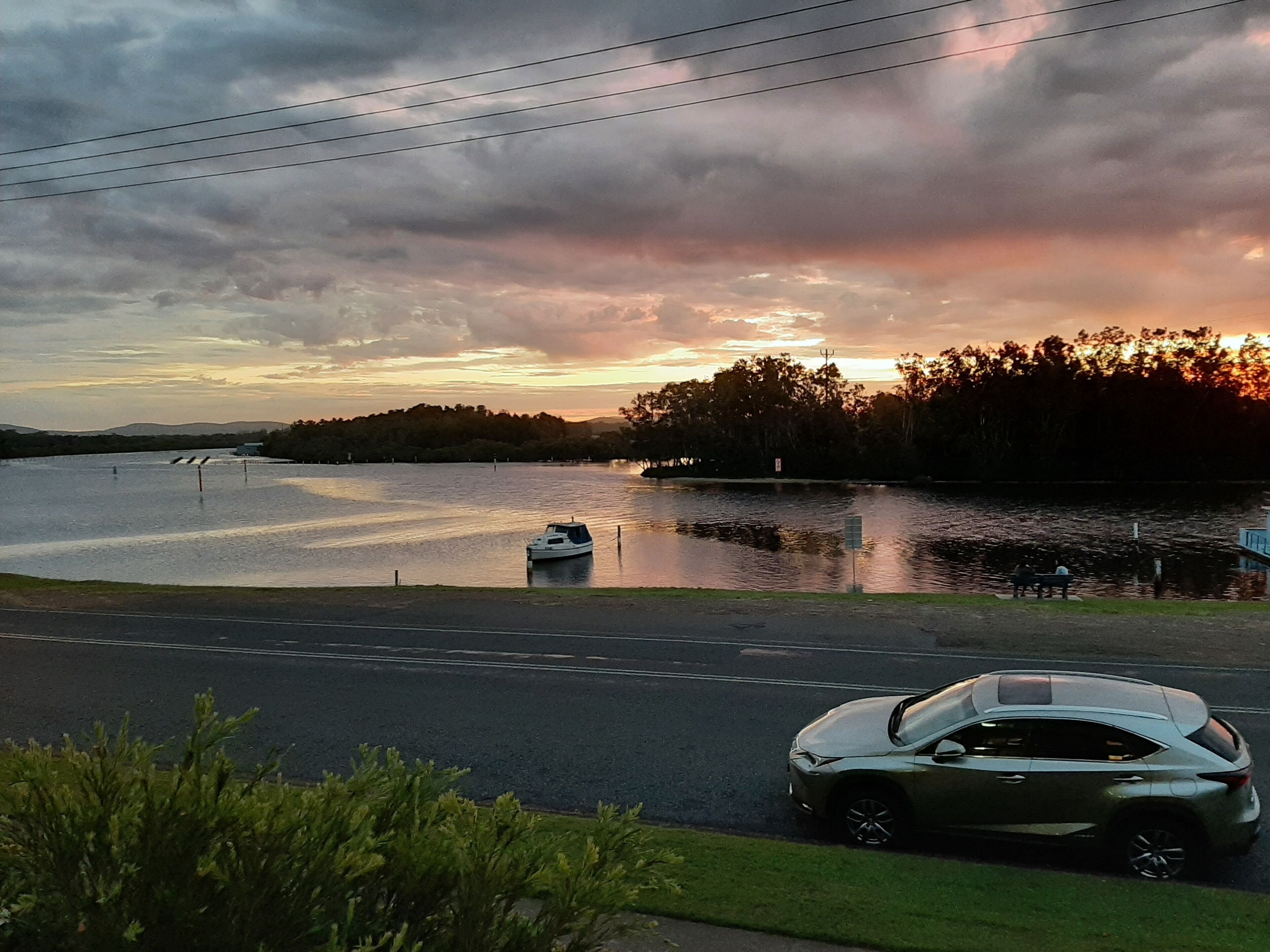 A car parked on a road with a body of water and trees in the background.
