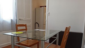 Ein Essbereich mit einem Glastisch, zwei Holzstühlen, einem gelben Teller und einer weißen Tür im Hintergrund.