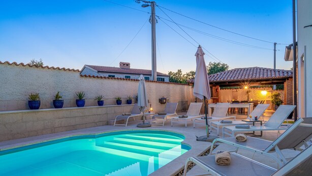 A swimming pool with lounge chairs and umbrellas, surrounded by potted plants and a tiled wall. - Villa Artist near Porec (Poreč)