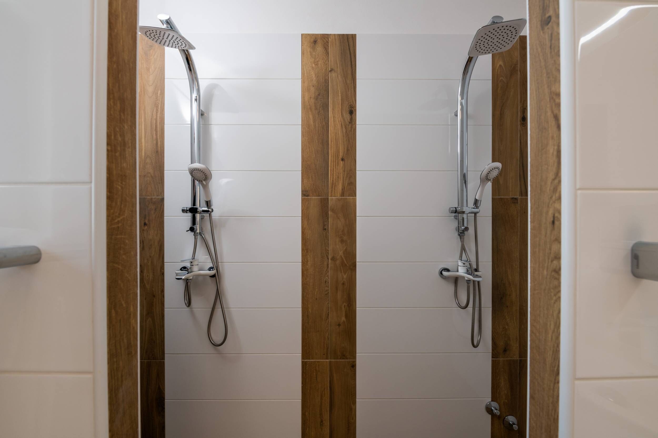 Ein Badezimmer mit zwei Duschen, Holzvertäfelung und weiß gefliesten Wänden.
