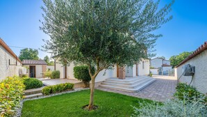 A courtyard with a tree, a small garden, and a pathway leading to a building with a tiled roof. - Villa Artist near Porec (Poreč)