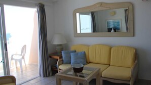 A living room with a yellow sofa, a glass coffee table, a lamp, and a mirror on the wall.