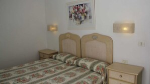 A bedroom with a double bed, two bedside tables, a nightstand, and a wall-mounted lamp.