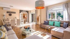 A modern living room with a sofa, coffee table, and a dining area with chairs and a table. - VILLA MIJAS PLAYA (AN)