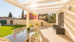 A covered patio with a table and chairs, a small lawn, and a building in the background. - VILLA MIJAS PLAYA (AN)