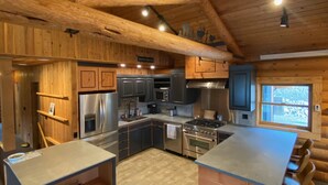 A spacious kitchen with wooden beams, stainless steel appliances, and a large island with bar stools. - Aspen Bear Paws | Charming Retreat with Hot Tub & Loft (Alpine)