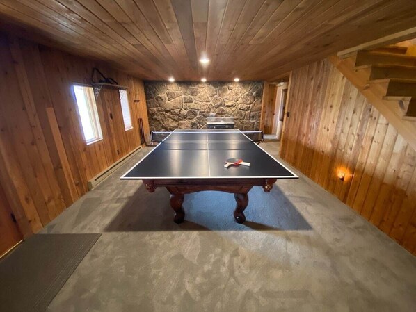 Une table de ping-pong dans une pièce aux murs en bois, avec un mur de pierre en arrière-plan.