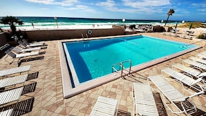 Una piscina rectangular con agua azul cristalina, rodeada de sillas de descanso y una terraza con baldosas.