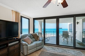 Relax in this stylish living room with a flat-screen TV, comfortable sofa, and sliding glass door leading to a balcony with ocean views.
