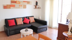 A living room with a black sofa, red and striped pillows, a small white table, and a lamp. - Argenta Caleta Apartaments (Peniscola)