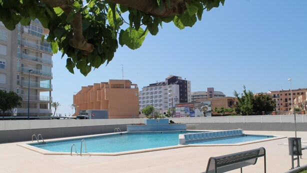 A swimming pool area with a bench, surrounded by buildings. - Argenta Caleta Apartaments (Peniscola)