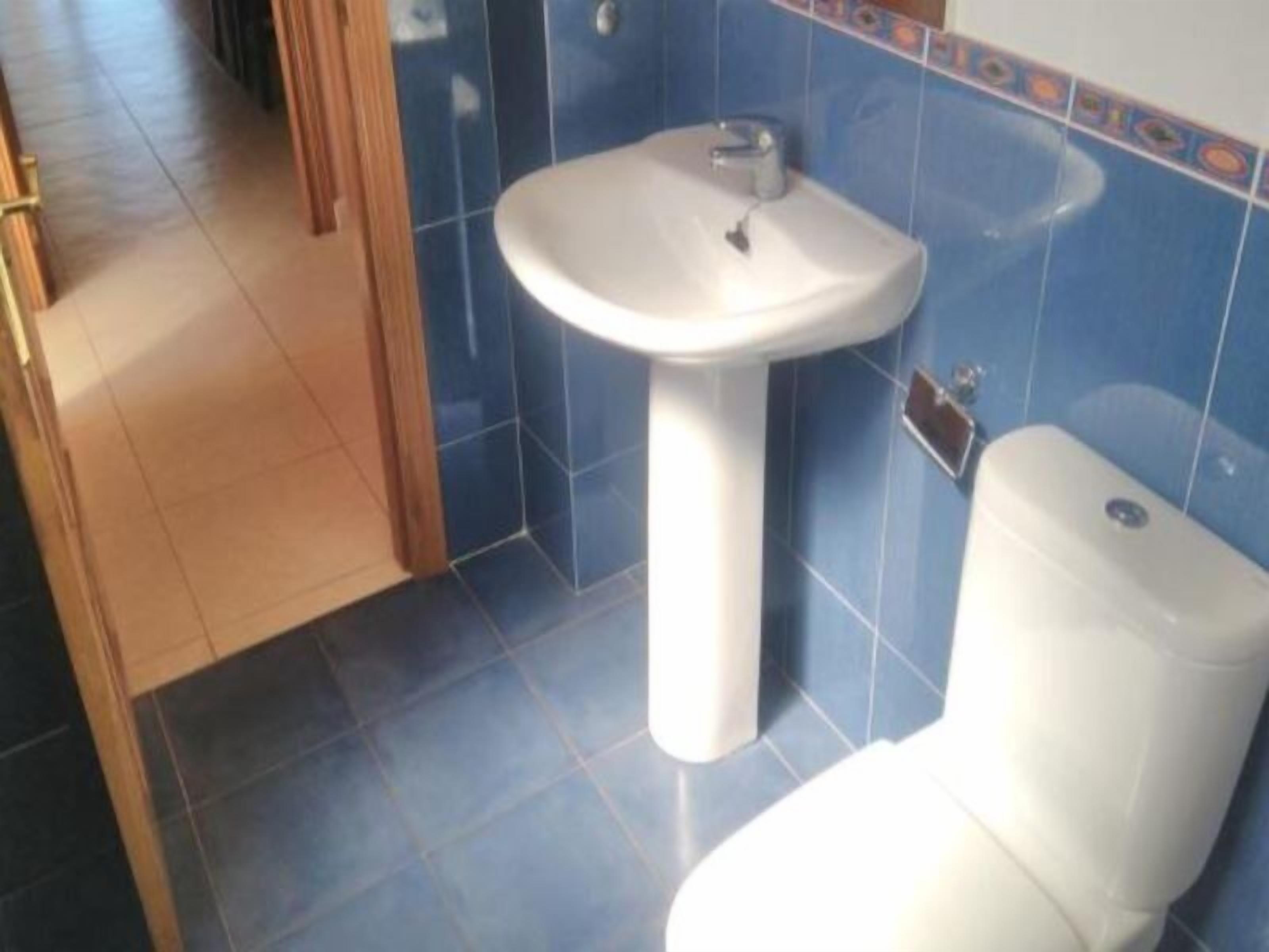 A bathroom with a white sink and toilet, blue tiled walls, and a wooden door.