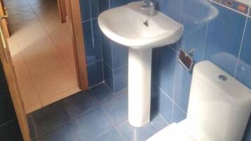 A bathroom with a white sink and toilet, blue tiled walls, and a wooden door.
