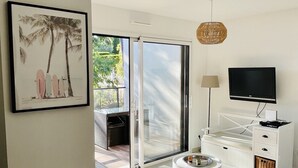 Un salon moderne comprenant un canapé, un téléviseur, une petite table et un balcon offrant une vue sur la verdure.