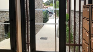 L’entrée d’un hôtel, avec une porte en verre à cadre noir, un mur en pierre et un espace de stationnement visible à travers la porte.