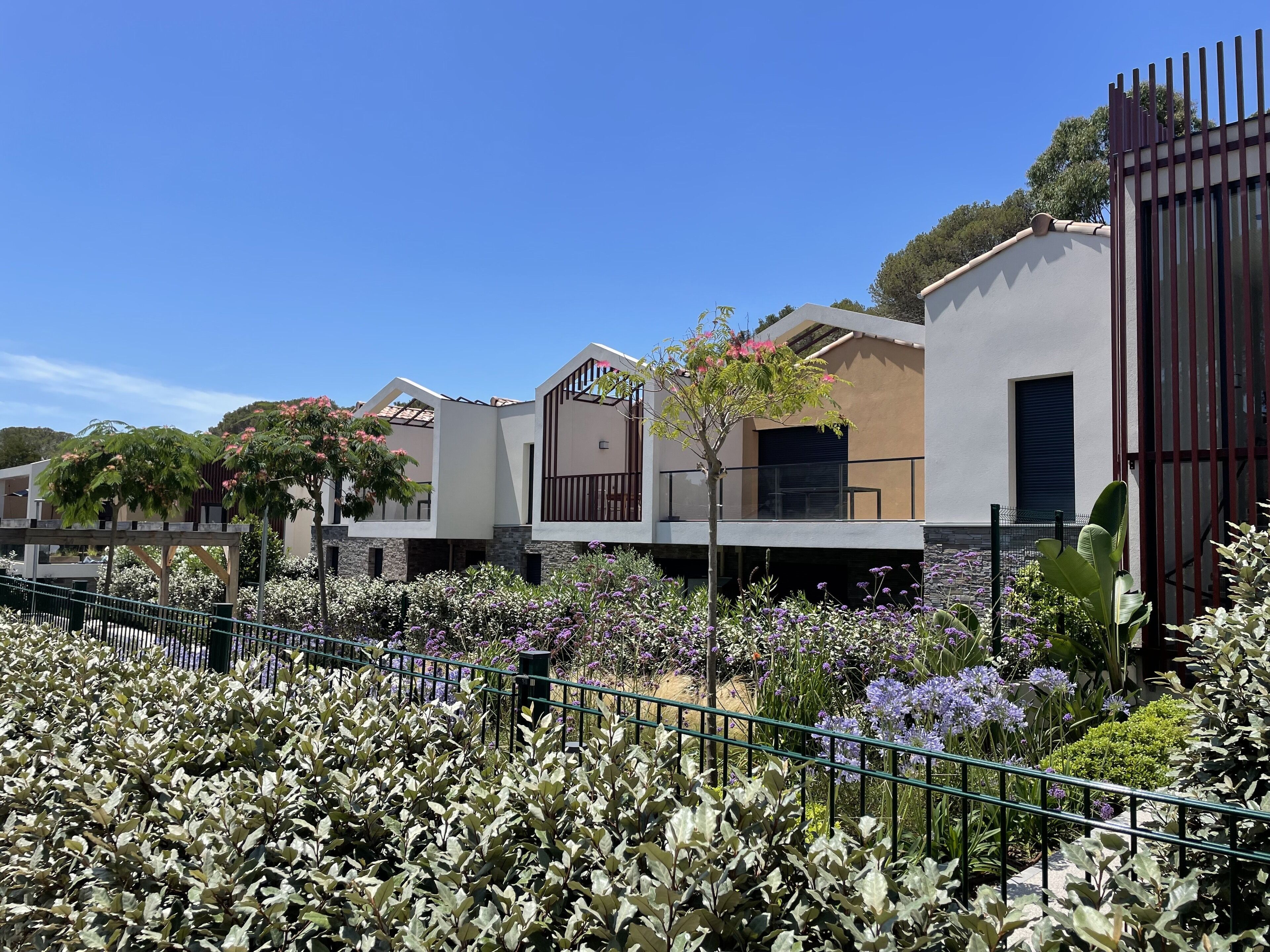 A row of modern houses with balconies, surrounded by a well-maintained garden with various plants and flowers.