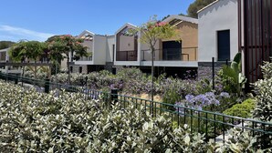 Une rangée de maisons modernes dotées de balcons, entourées d’un jardin bien entretenu où poussent différentes plantes et fleurs.