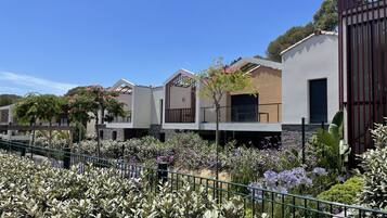 A row of modern houses with balconies, surrounded by a well-maintained garden with various plants and flowers.