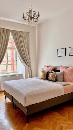 A bedroom with a large bed, a chandelier, a window with curtains, and a radiator.
