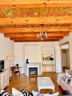 A living room with a fireplace, wooden ceiling, and a chandelier.