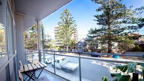 A balcony with a view of a street, a parked truck, and a building in the background. - Manly Oceanside (Sydney)